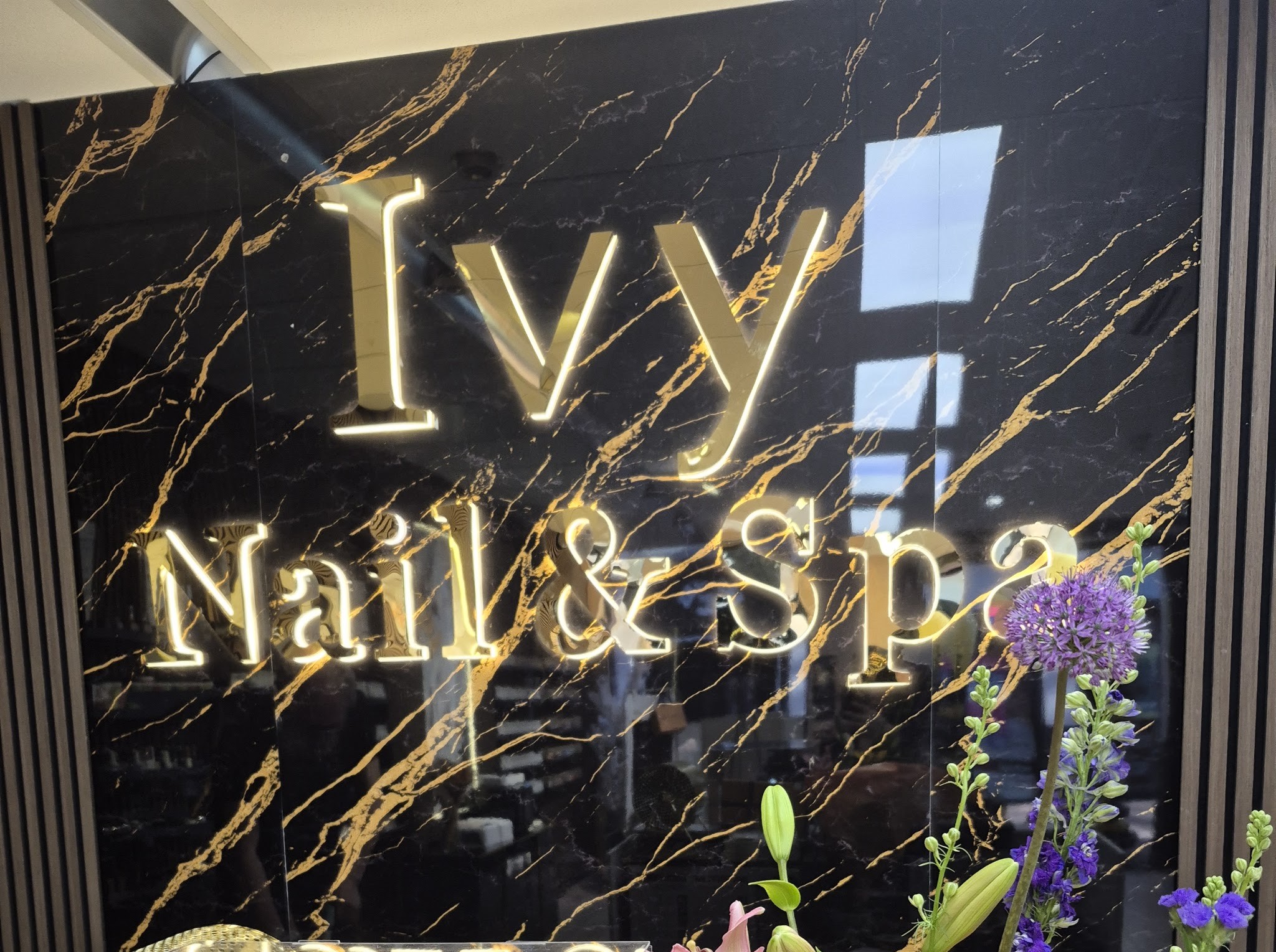 Het verlichte gouden naambord van Ivy Nail en Spa op de marmeren wand